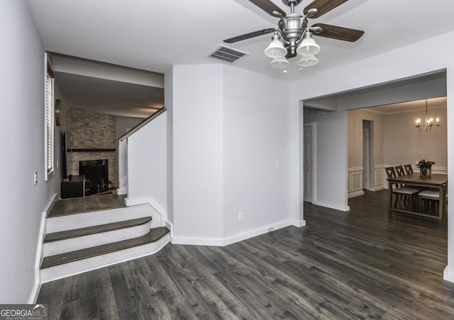 interior space with ceiling fan with notable chandelier, a stone fireplace, wood finished floors, and visible vents