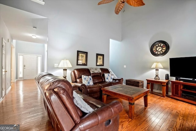 living room with light wood-style floors, a towering ceiling, and a ceiling fan