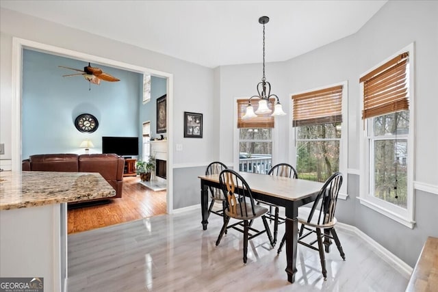 dining space with a fireplace, ceiling fan with notable chandelier, baseboards, and light wood-type flooring