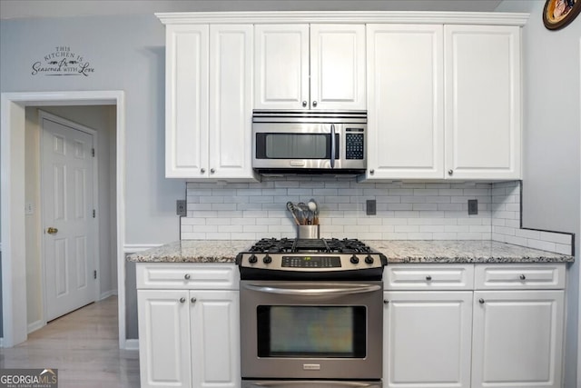 kitchen with light wood finished floors, backsplash, light stone counters, white cabinets, and stainless steel appliances