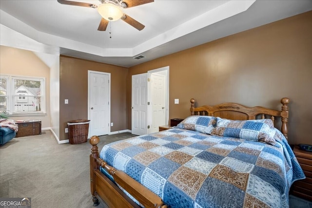 bedroom with a ceiling fan, visible vents, baseboards, carpet floors, and a tray ceiling