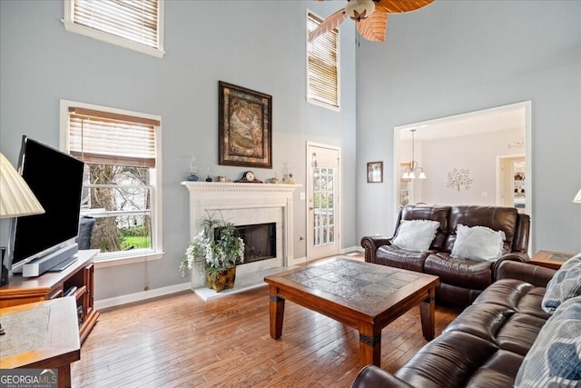 living area with a towering ceiling, wood-type flooring, a premium fireplace, baseboards, and ceiling fan