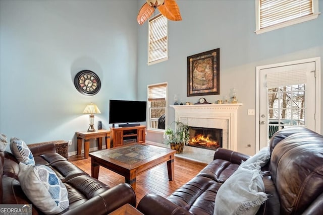 living area with wood finished floors, baseboards, a towering ceiling, and a premium fireplace