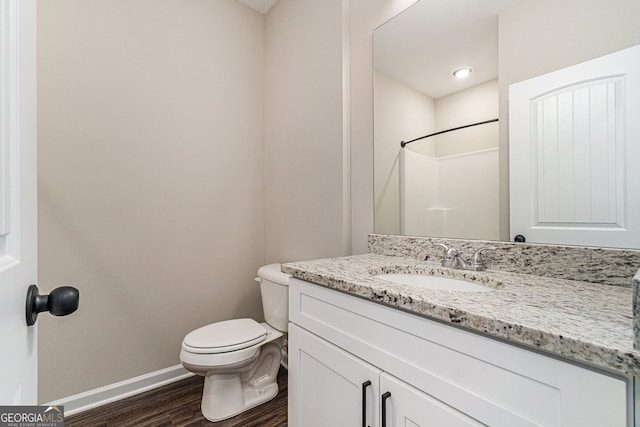 bathroom with toilet, wood finished floors, vanity, baseboards, and a shower