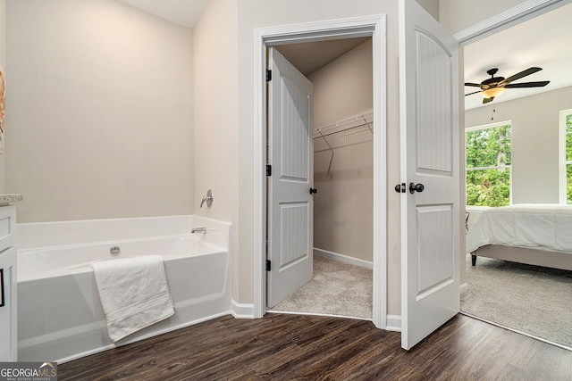 bathroom with ensuite bathroom, ceiling fan, wood finished floors, baseboards, and a bath