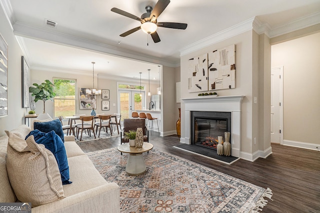 living area featuring dark wood-style floors, a glass covered fireplace, crown molding, and baseboards