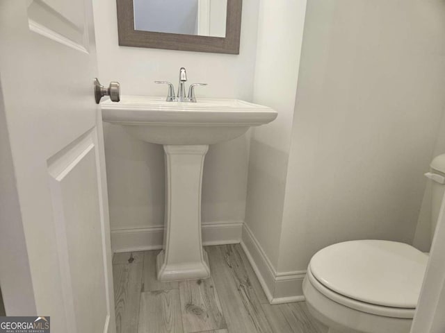 half bathroom with a sink, wood finished floors, toilet, and baseboards