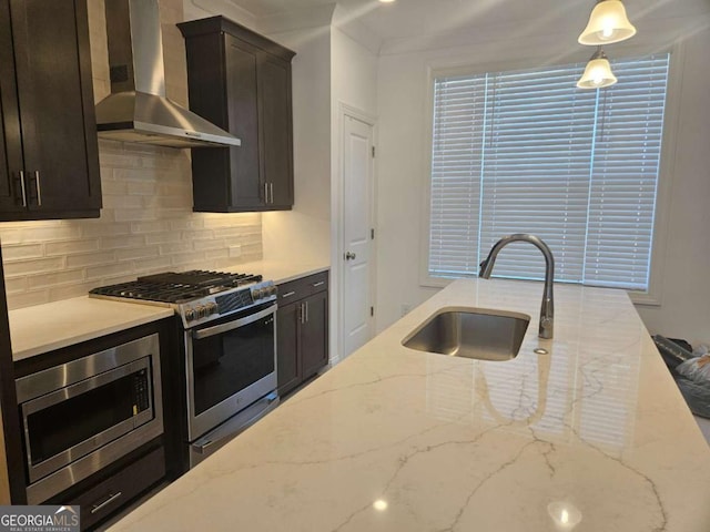 kitchen featuring light stone counters, stainless steel appliances, backsplash, a sink, and wall chimney exhaust hood