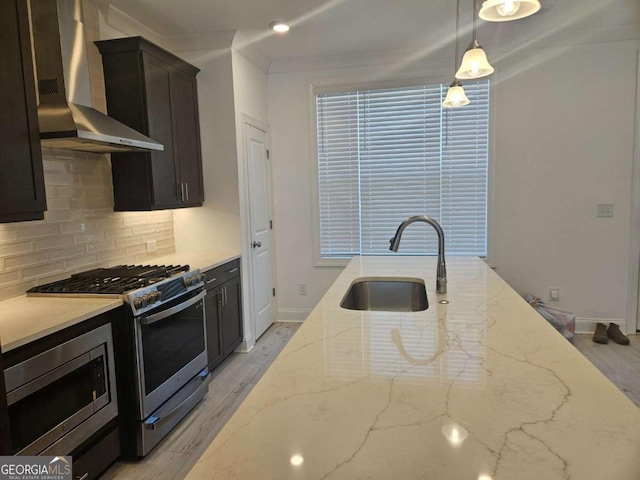 kitchen featuring wall chimney exhaust hood, a sink, light stone countertops, stainless steel appliances, and backsplash