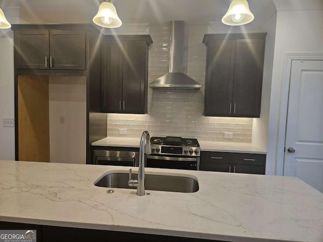 kitchen featuring light stone counters, a sink, wall chimney range hood, backsplash, and stainless steel gas stove