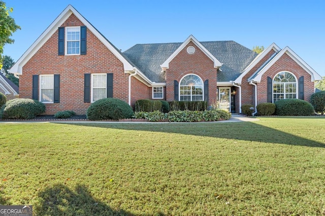 traditional-style home with brick siding, a front yard, and roof with shingles