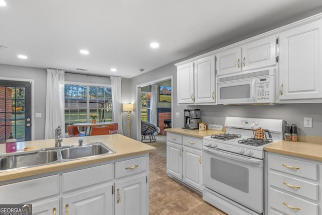 kitchen with a sink, recessed lighting, white appliances, white cabinets, and light countertops