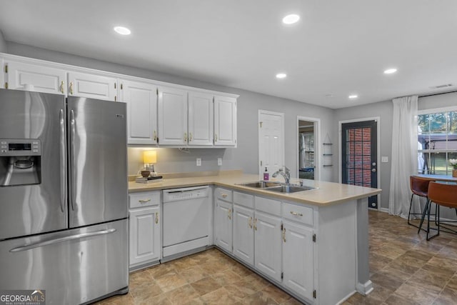 kitchen featuring a peninsula, a sink, light countertops, dishwasher, and stainless steel fridge