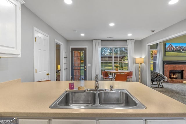 kitchen featuring a sink, a brick fireplace, recessed lighting, and white cabinetry