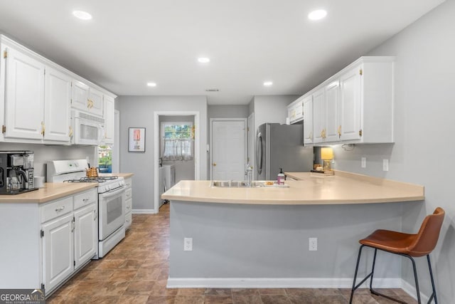 kitchen featuring a sink, white cabinetry, recessed lighting, white appliances, and a peninsula