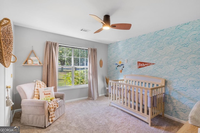 carpeted bedroom with visible vents, wallpapered walls, a crib, an accent wall, and baseboards