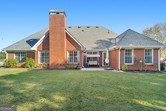 rear view of house with a lawn, a patio, roof with shingles, brick siding, and a chimney