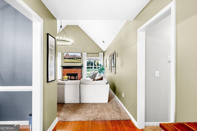 hallway featuring baseboards, lofted ceiling, an inviting chandelier, and wood finished floors