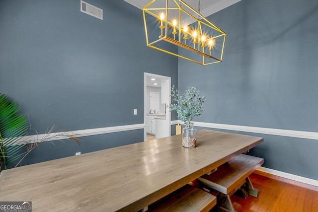 dining space featuring visible vents, crown molding, baseboards, a towering ceiling, and wood finished floors