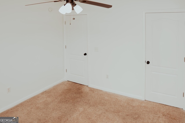 empty room featuring light colored carpet, baseboards, and a ceiling fan