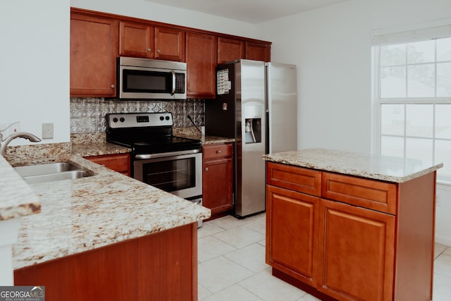 kitchen with a sink, stainless steel appliances, light tile patterned floors, decorative backsplash, and light stone countertops