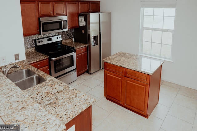 kitchen with a sink, tasteful backsplash, a center island, stainless steel appliances, and light stone countertops