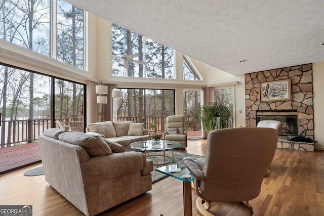 living room with a high ceiling, a stone fireplace, a textured ceiling, and wood finished floors