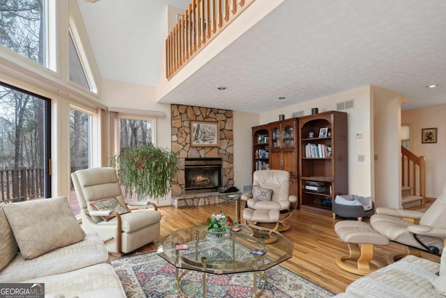 living area with a wealth of natural light, a stone fireplace, wood finished floors, and visible vents