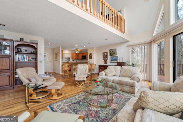 living room with a towering ceiling, light wood-style floors, a ceiling fan, and recessed lighting