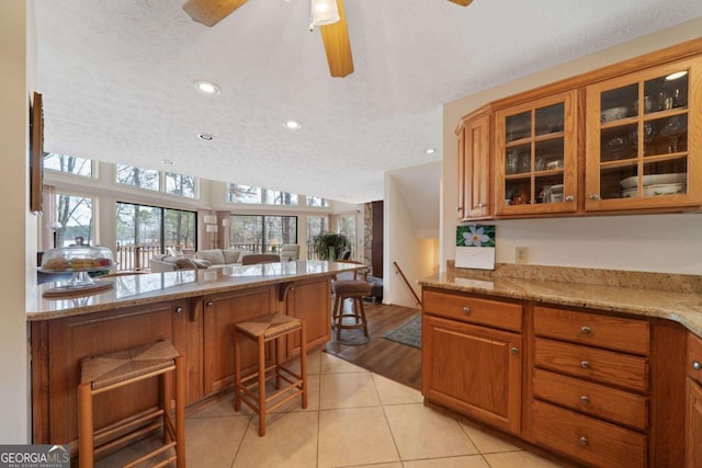 kitchen featuring light tile patterned floors, glass insert cabinets, a breakfast bar area, brown cabinets, and open floor plan