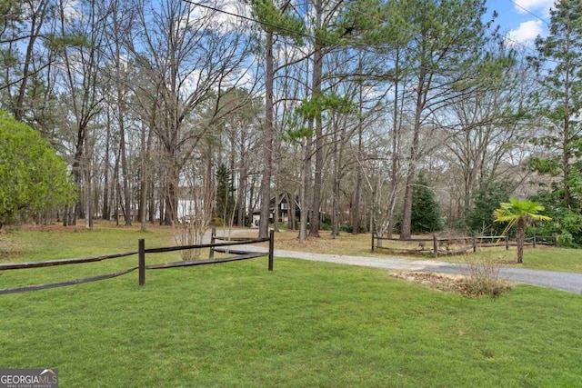 view of community featuring dirt driveway, fence, and a yard