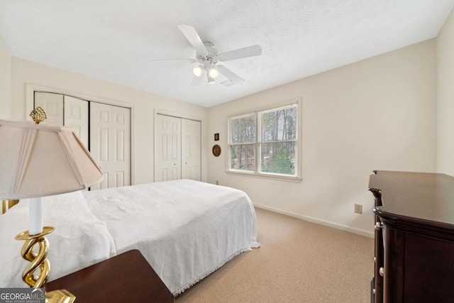 bedroom with ceiling fan, a textured ceiling, light carpet, baseboards, and two closets