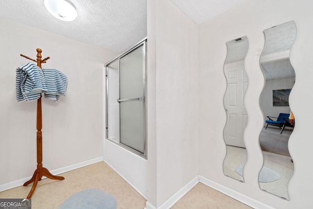 full bath with a textured ceiling, combined bath / shower with glass door, and baseboards