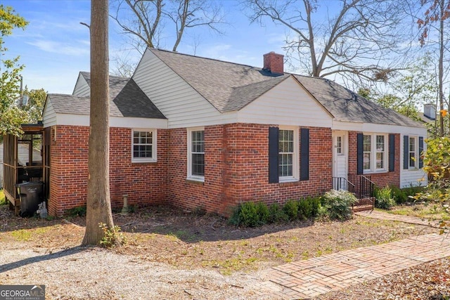 view of front facade featuring brick siding, a chimney, and a shingled roof