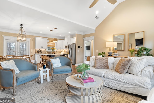 living area featuring visible vents, light wood-style flooring, ornamental molding, high vaulted ceiling, and ceiling fan with notable chandelier