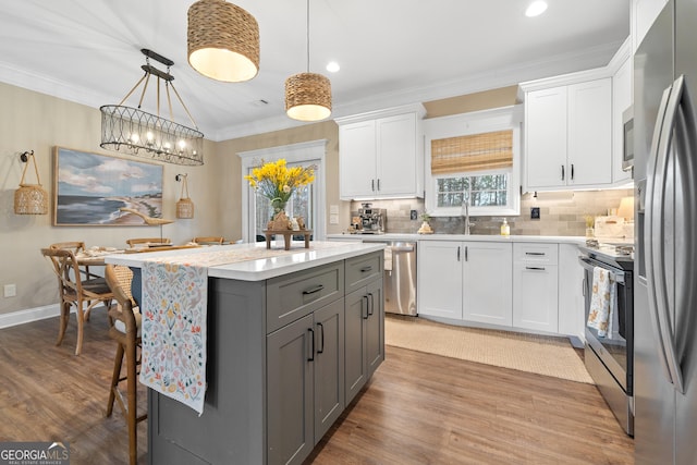 kitchen featuring crown molding, gray cabinets, appliances with stainless steel finishes, a sink, and a kitchen bar