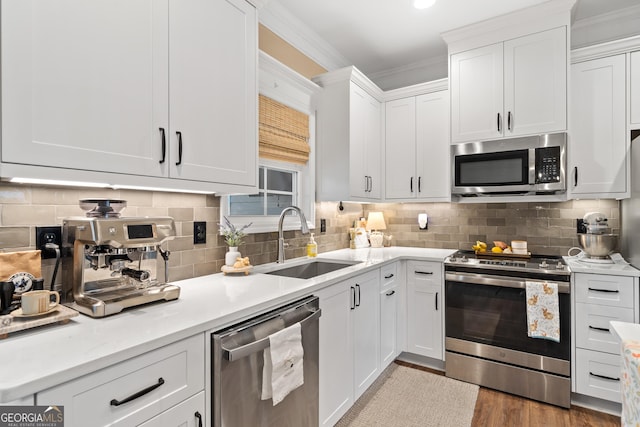 kitchen featuring a sink, white cabinets, light countertops, appliances with stainless steel finishes, and crown molding