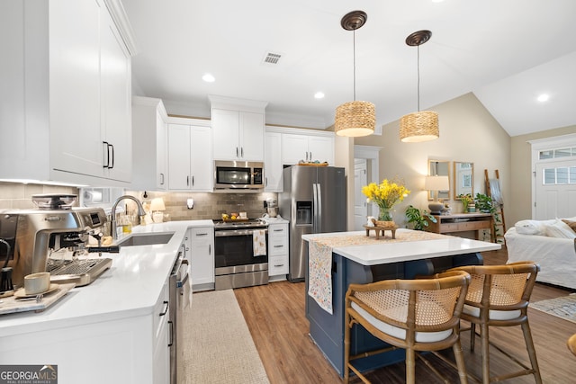 kitchen with stainless steel appliances, a kitchen island, a sink, light countertops, and tasteful backsplash