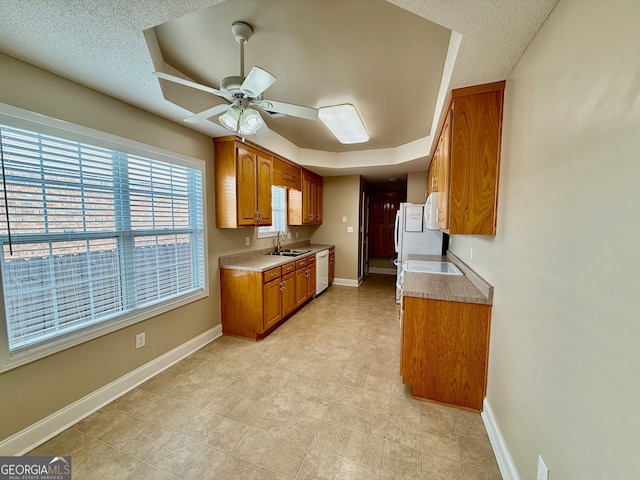 kitchen with white appliances, baseboards, ceiling fan, brown cabinets, and a sink