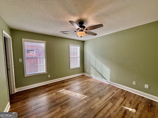 spare room featuring visible vents, hardwood / wood-style floors, ceiling fan, a textured ceiling, and baseboards