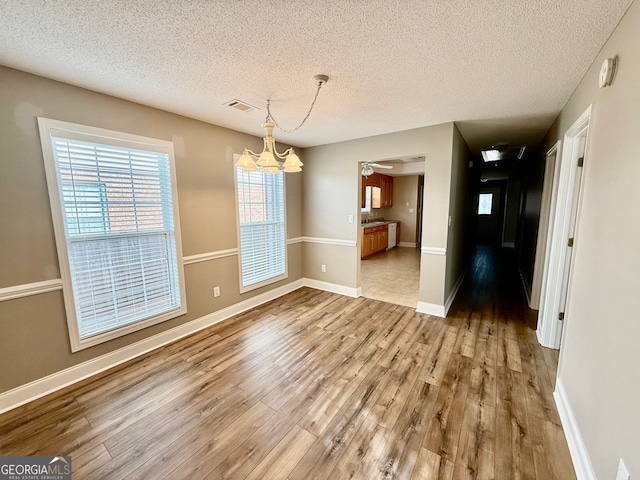 unfurnished dining area featuring baseboards, a notable chandelier, visible vents, and wood finished floors