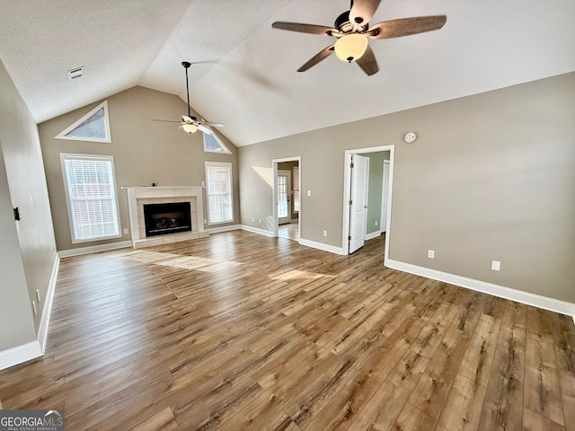 unfurnished living room with ceiling fan, a tiled fireplace, wood finished floors, and a wealth of natural light