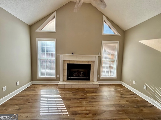 unfurnished living room featuring baseboards, a fireplace with raised hearth, wood finished floors, a textured ceiling, and high vaulted ceiling