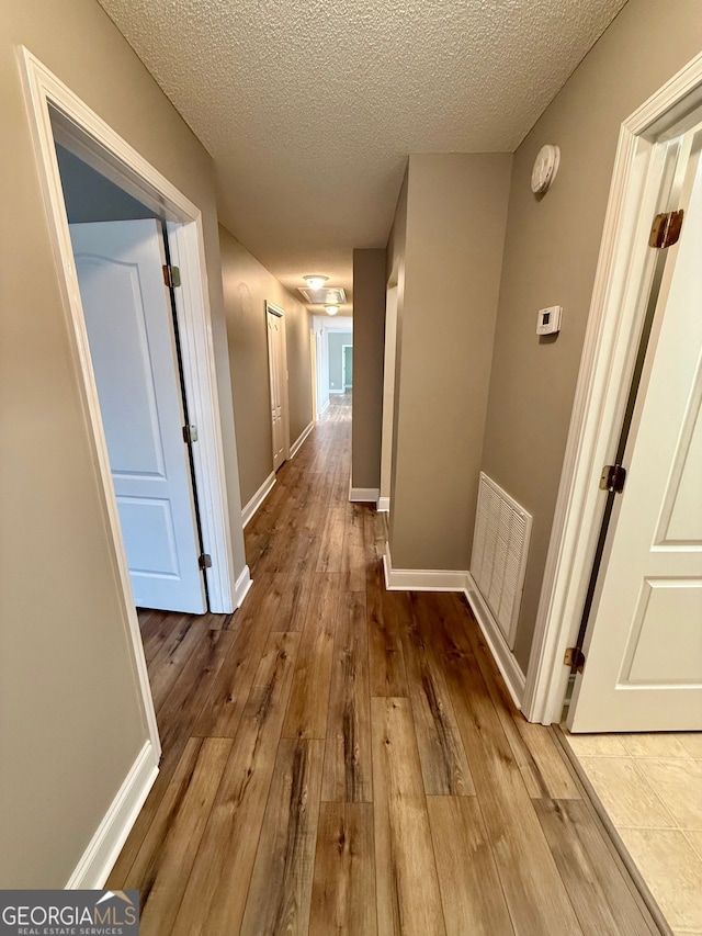 corridor with a textured ceiling, hardwood / wood-style floors, visible vents, and baseboards