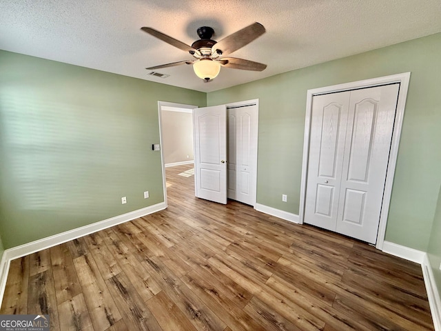 unfurnished bedroom featuring wood finished floors, two closets, visible vents, and baseboards