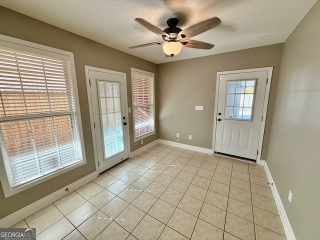 doorway featuring a ceiling fan, a textured ceiling, baseboards, and light tile patterned floors