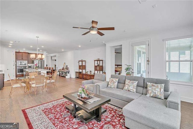 living area featuring recessed lighting, light wood finished floors, and ceiling fan with notable chandelier