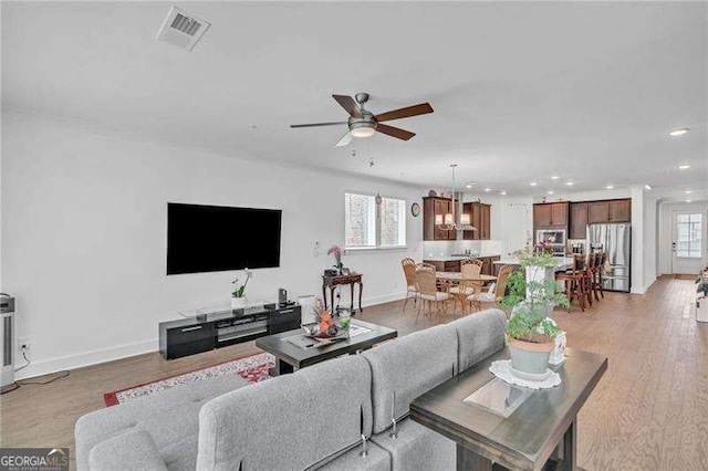 living area with light wood-style floors, visible vents, ceiling fan, and baseboards