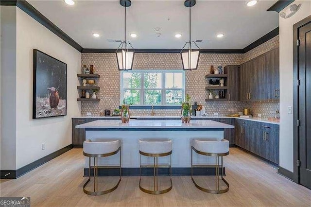 kitchen with a kitchen island, ornamental molding, a kitchen breakfast bar, light countertops, and open shelves