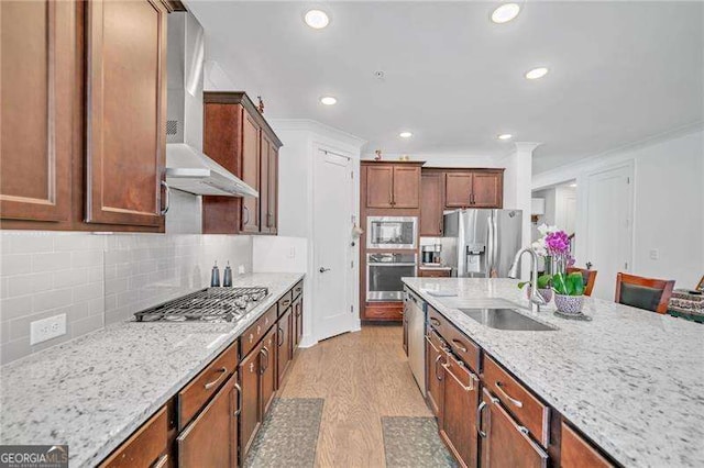 kitchen featuring stainless steel appliances, tasteful backsplash, light wood-style flooring, a sink, and wall chimney exhaust hood